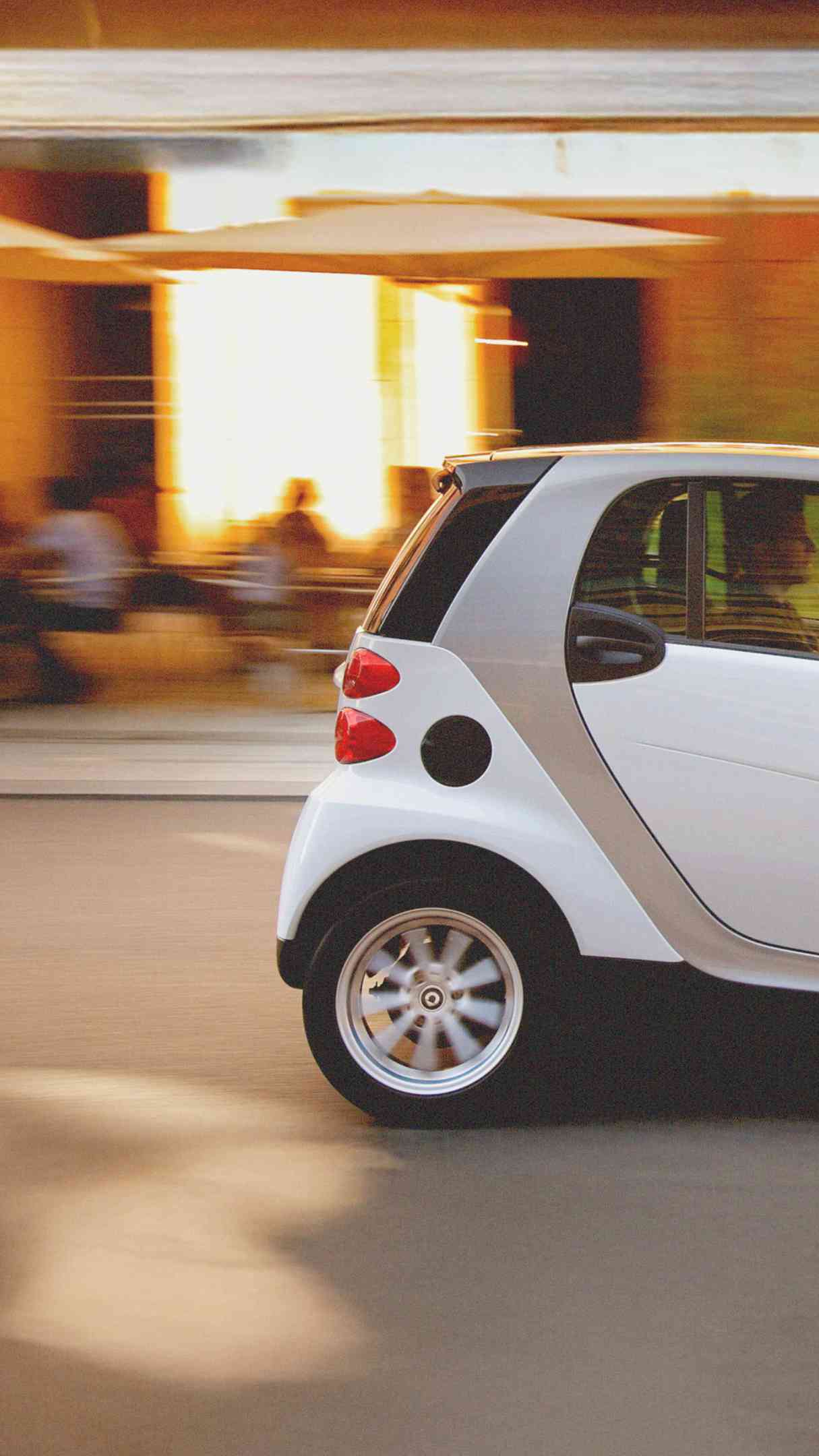 Ein weißer smart fortwo fährt an einem Café vorbei.