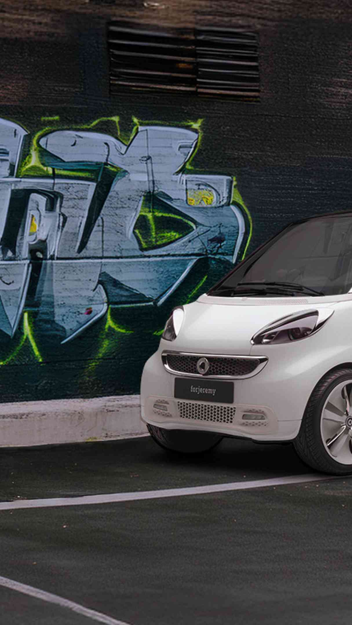 Ein weißer smart forjeremy vor einer mit Graffitti besprühten Wand.