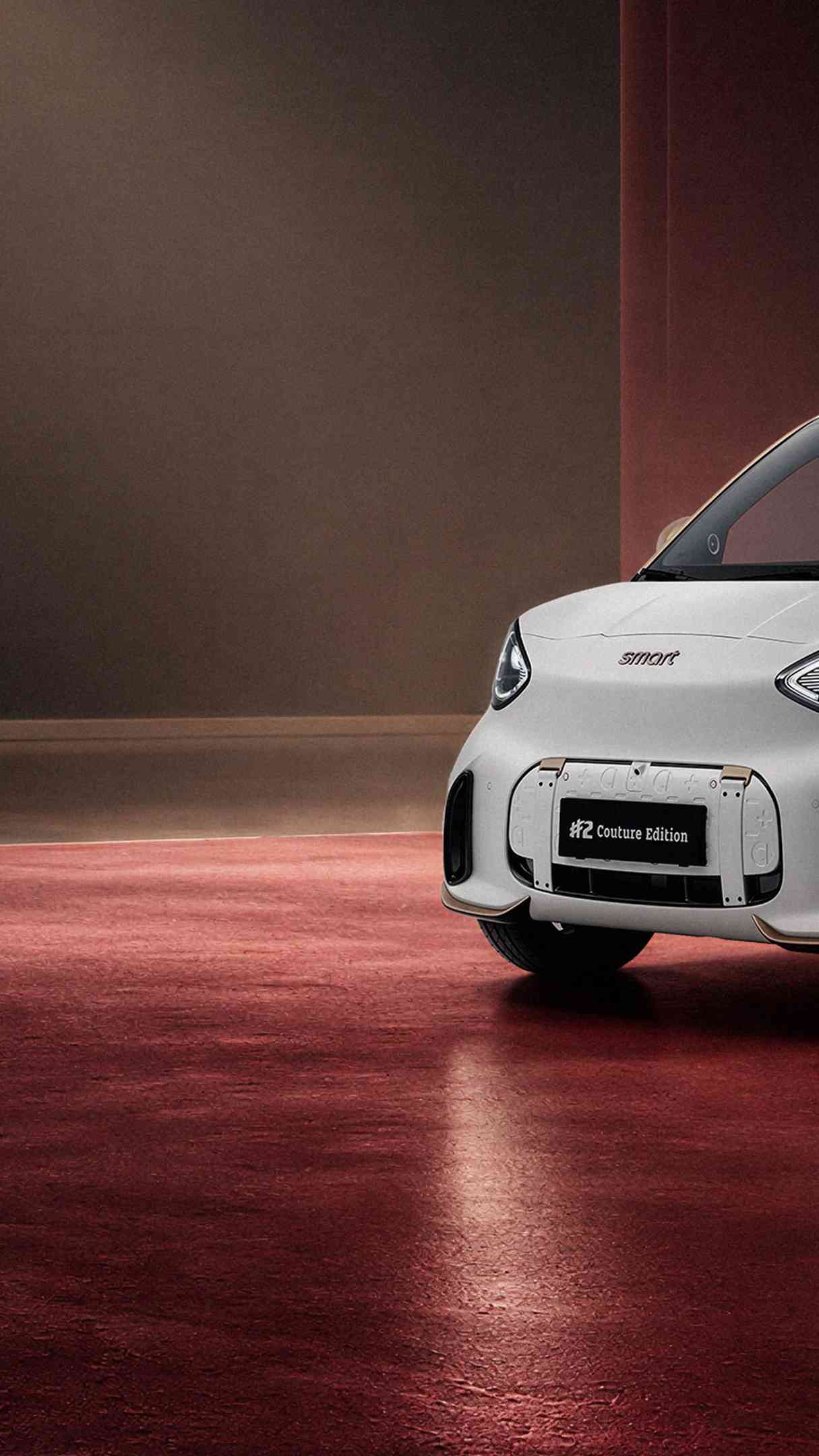 Um smart #2 Couture Edition em branco mate e com teto dourado está num palco e é iluminado de cima, em ângulo oblíquo.