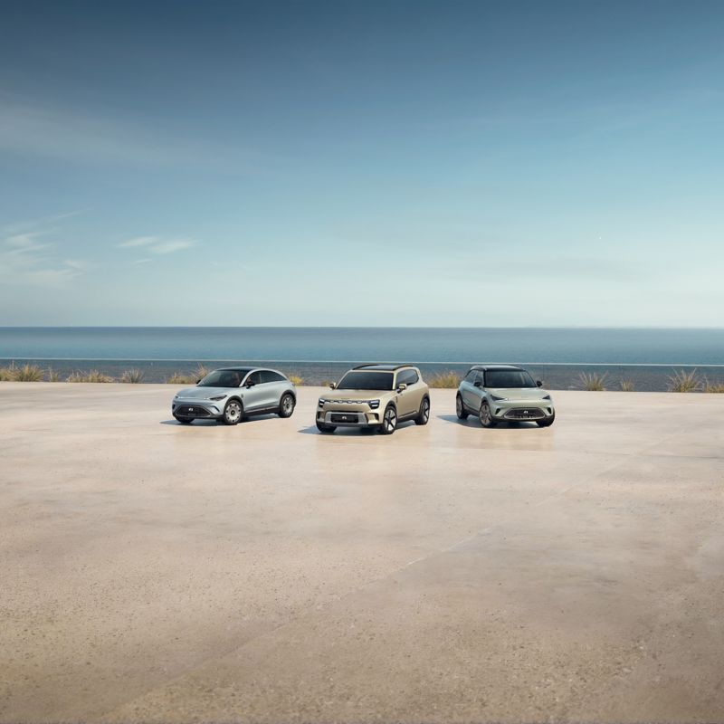 Zwei smart Autos vor einem minimalistischen Gebäude mit Bäumen im Hintergrund.