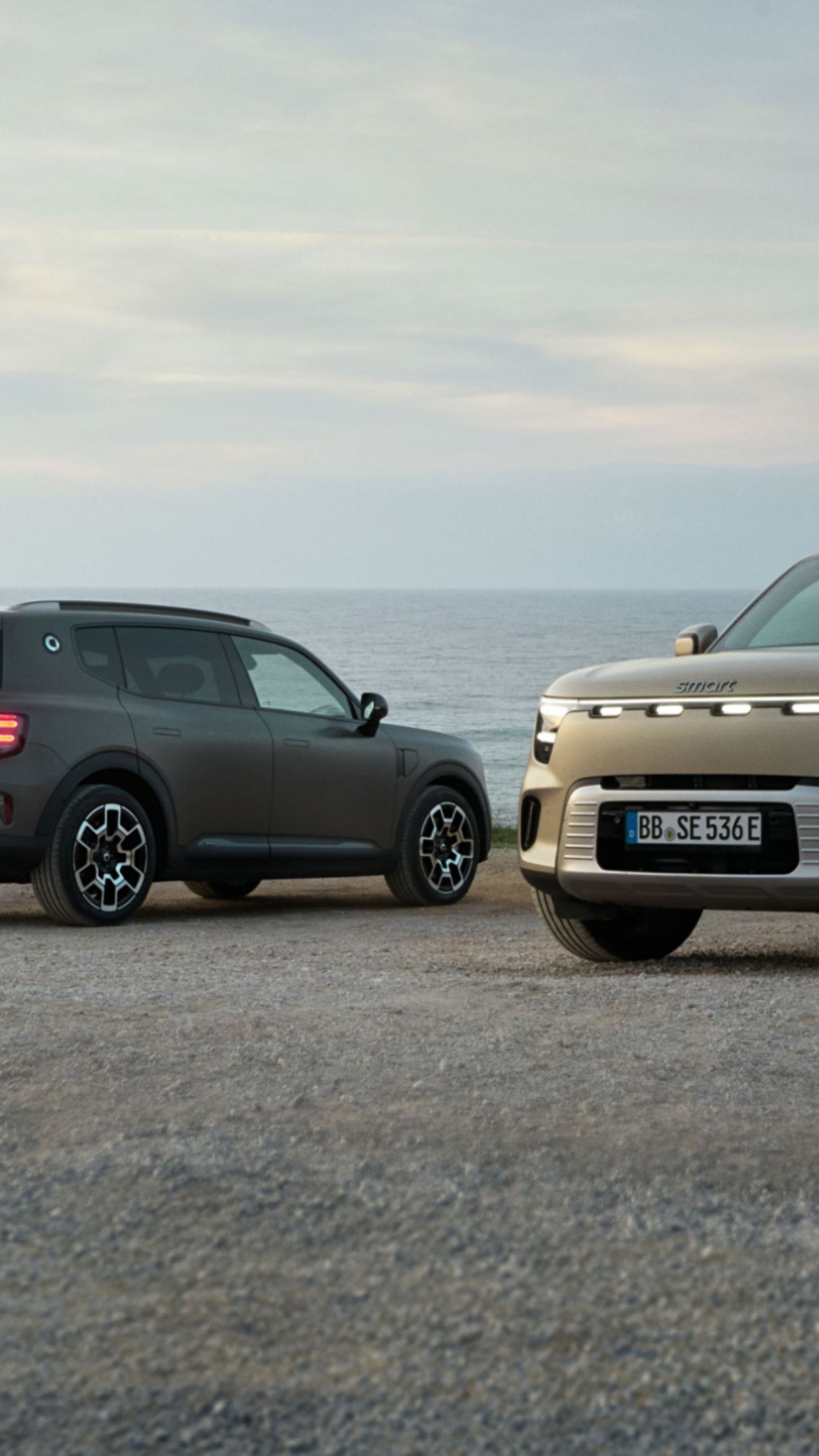 Due smart #5 sono posizionate l’una all'opposto dell’altra in un parcheggio accanto al mare.