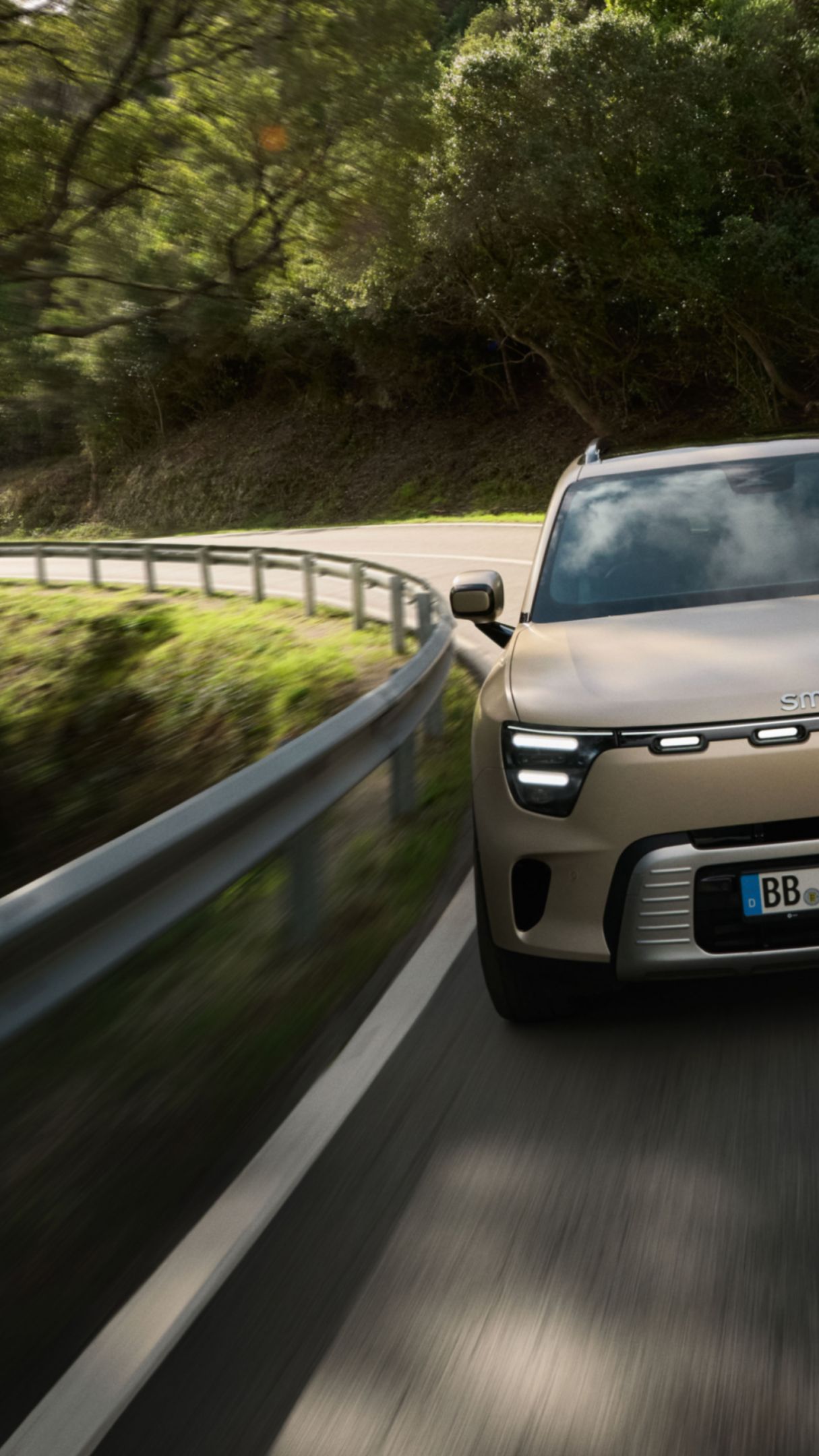 Una smart #5 percorre una strada tortuosa e parzialmente ombreggiata da alberi.