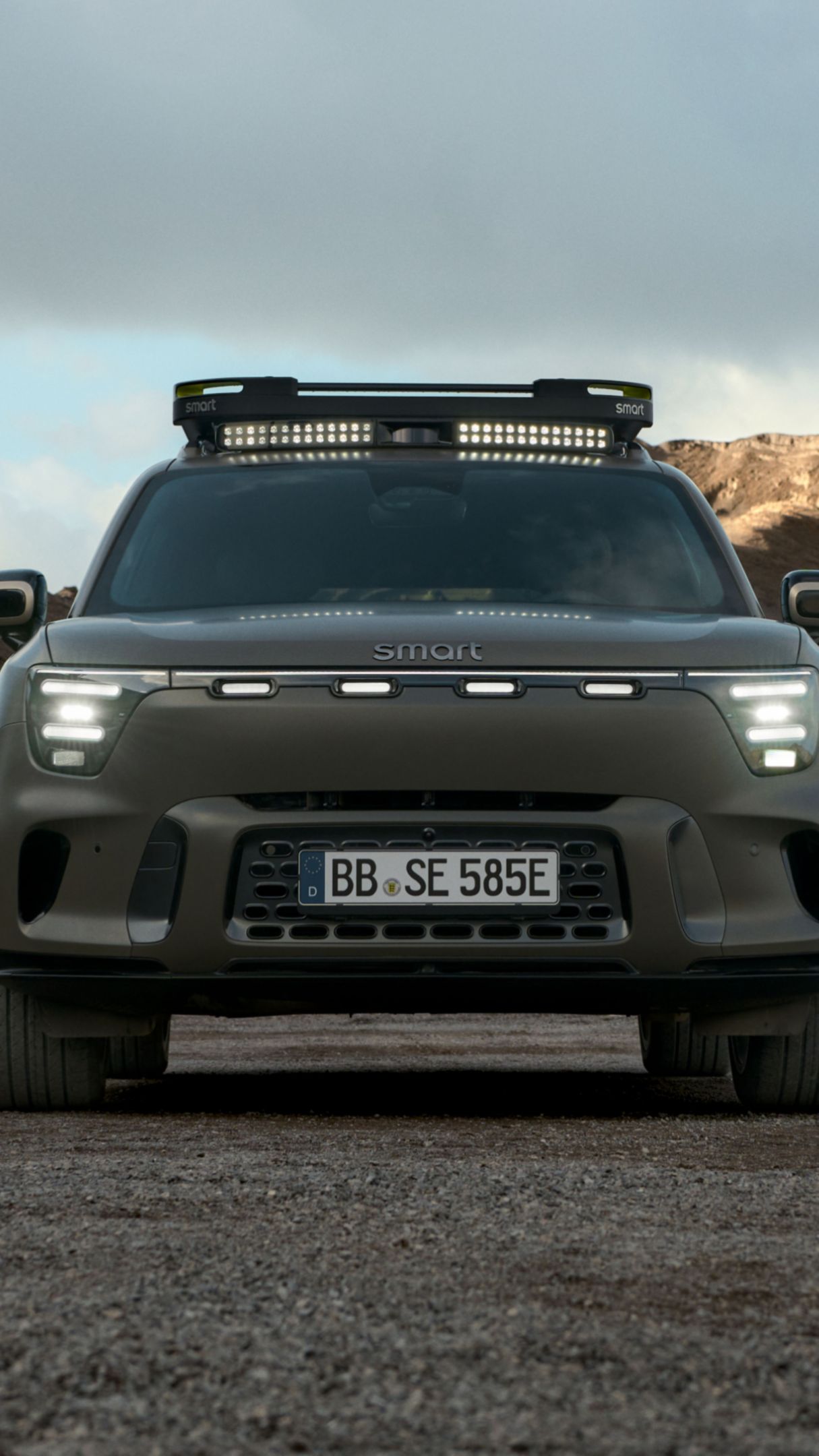 Front view of the smart #5, with large, rocky hills in the background under a cloudy sky.